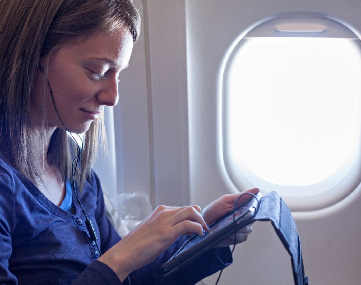 A woman is looking at her tablet on an airplane.